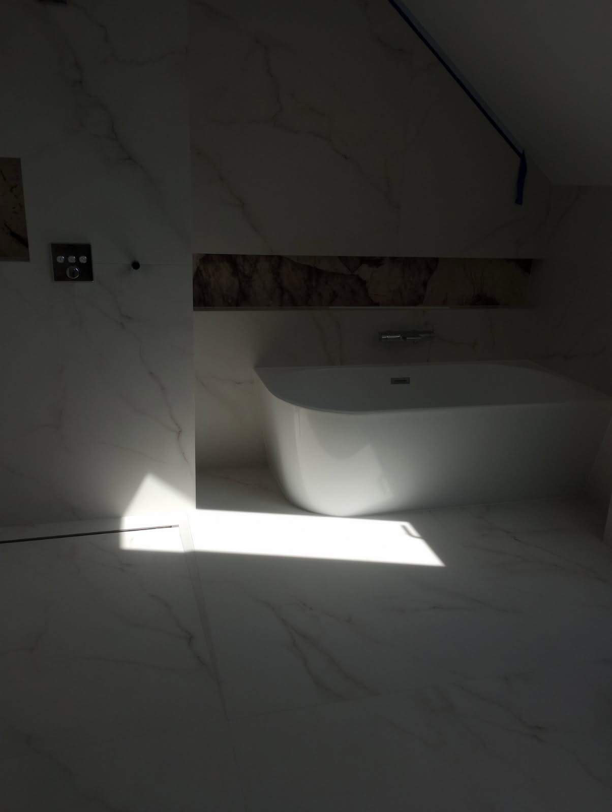 Nowoczesna, wolnostojąca wanna w łazience wykończonej białym marmurem, z dekoracyjną wnęką nad wanną i punktowym oświetleniem.
