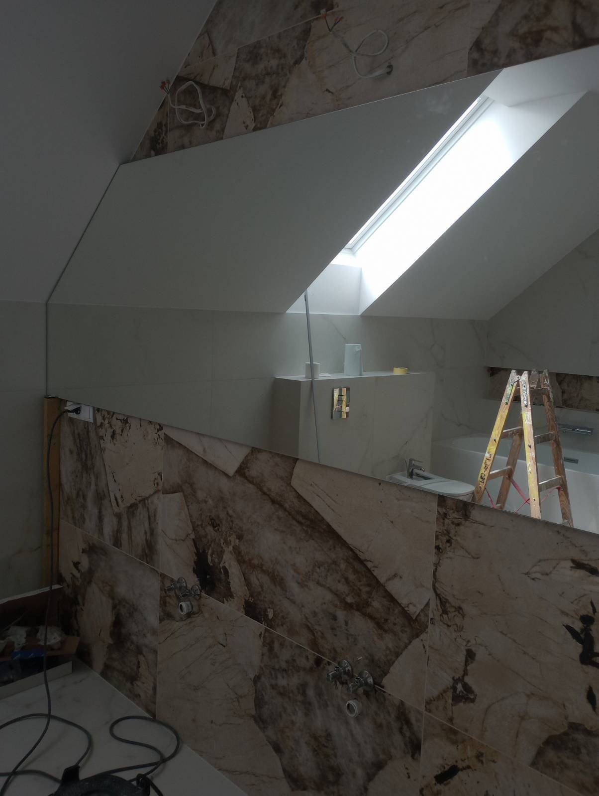 Łazienka w trakcie remontu na poddaszu, widoczne płytki imitujące marmur, drabina i okno dachowe.