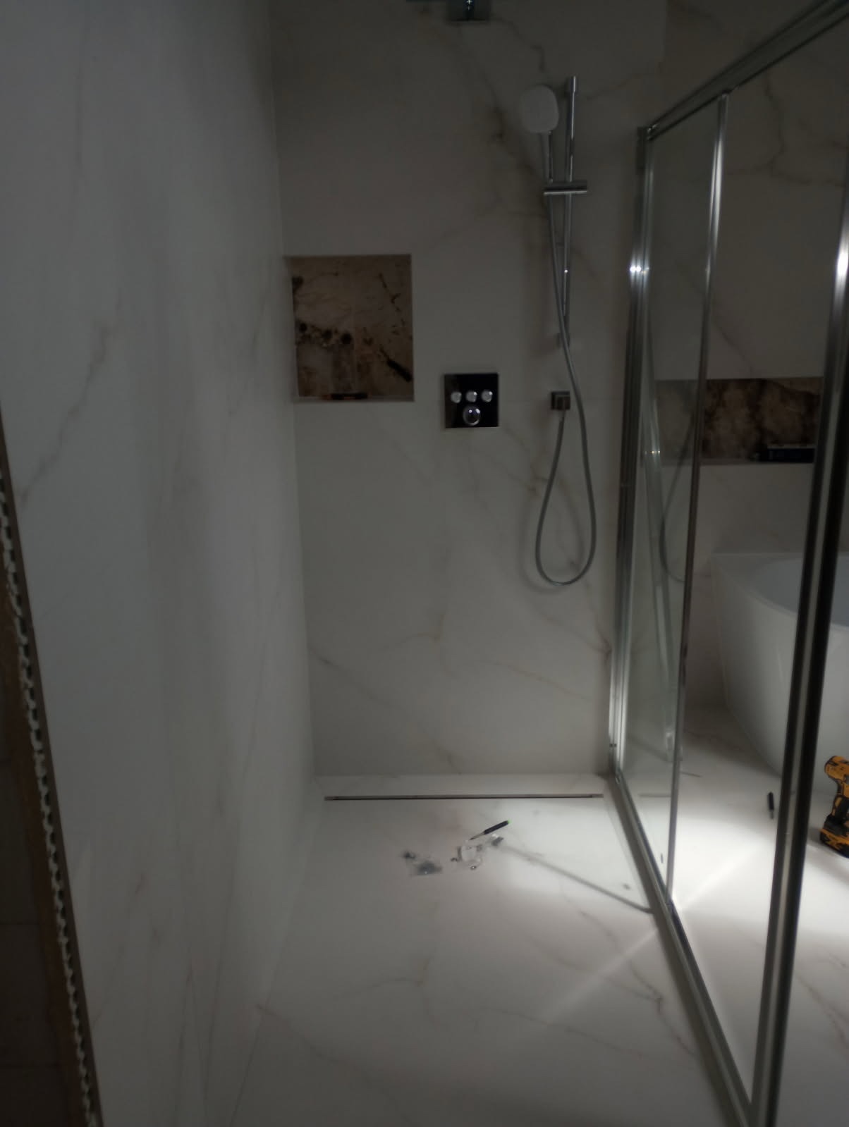 Nowoczesna kabina prysznicowa z marmurowymi ścianami, widoczne elementy montażowe na podłodze i narzędzie w rogu, sugerujące trwający montaż.