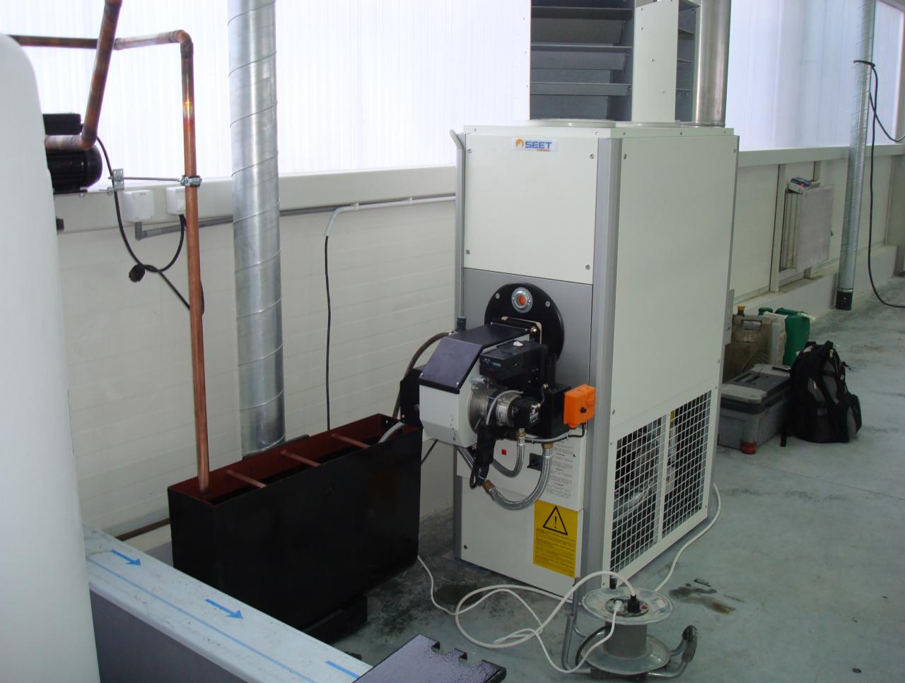 Biała centrala wentylacyjna z palnikiem w Szczecinie. Widoczny fragment instalacji, przewody i skrzynka. Urządzenie SEET w pomieszczeniu.