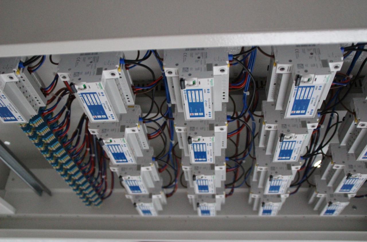 Szereg zabezpieczeń elektrycznych zamontowanych w rozdzielni, widoczne kable i złączki, instalacja pod sufitem.