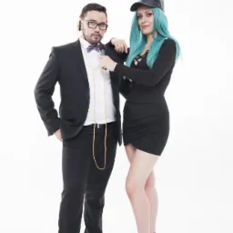 Duet muzyczny z Warszawy: mężczyzna w garniturze z muszką i słuchawkami, kobieta w czarnej sukience i czapce z turkusowymi włosami, oboje z mikrofonem na białym tle.