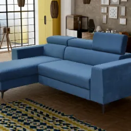 Narożnik tapicerowany w odcieniach błękitu z regulowanymi zagłówkami, ustawiony na drewnianej podłodze z wzorzystym dywanem, w tle okno z widokiem na zieleń i dekoracyjne elementy wystroju.