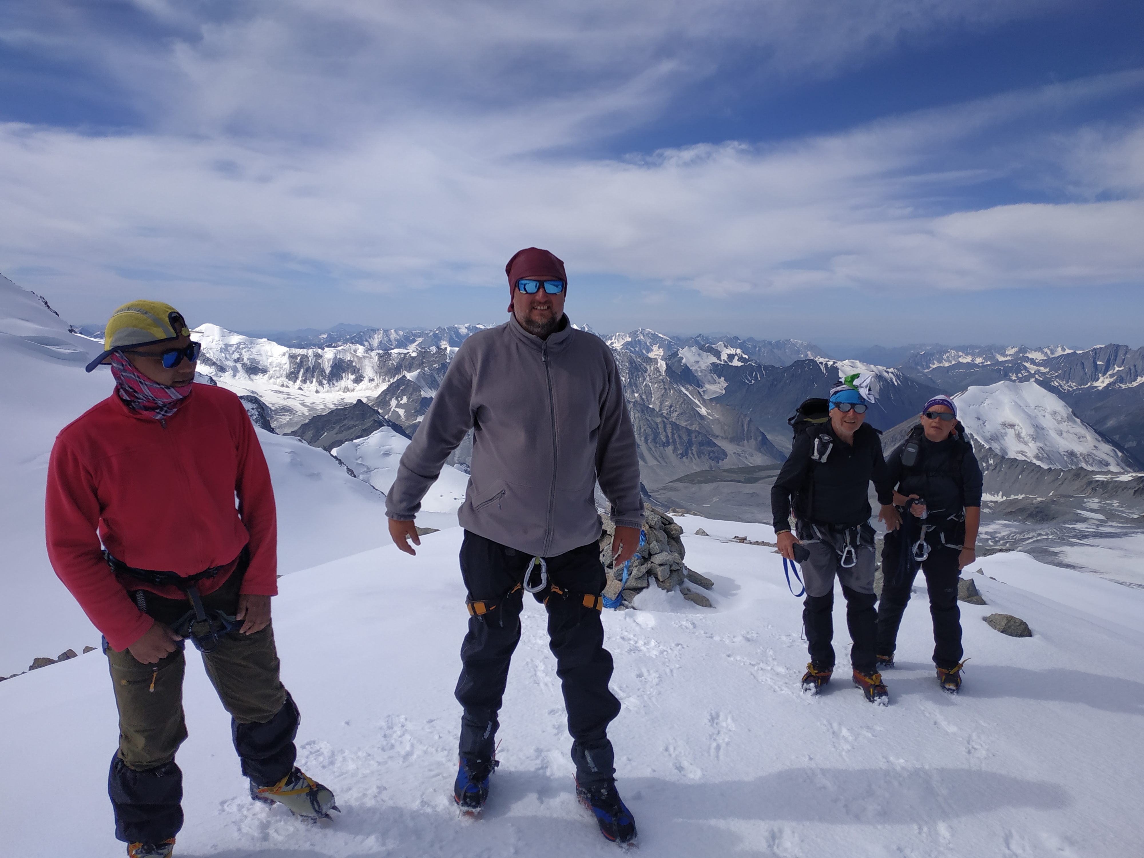 Grupa turystów wspinających się na ośnieżony szczyt górski w Mongolii, widoczne raki na butach, uprzęże i liny, w tle rozległa panorama gór.