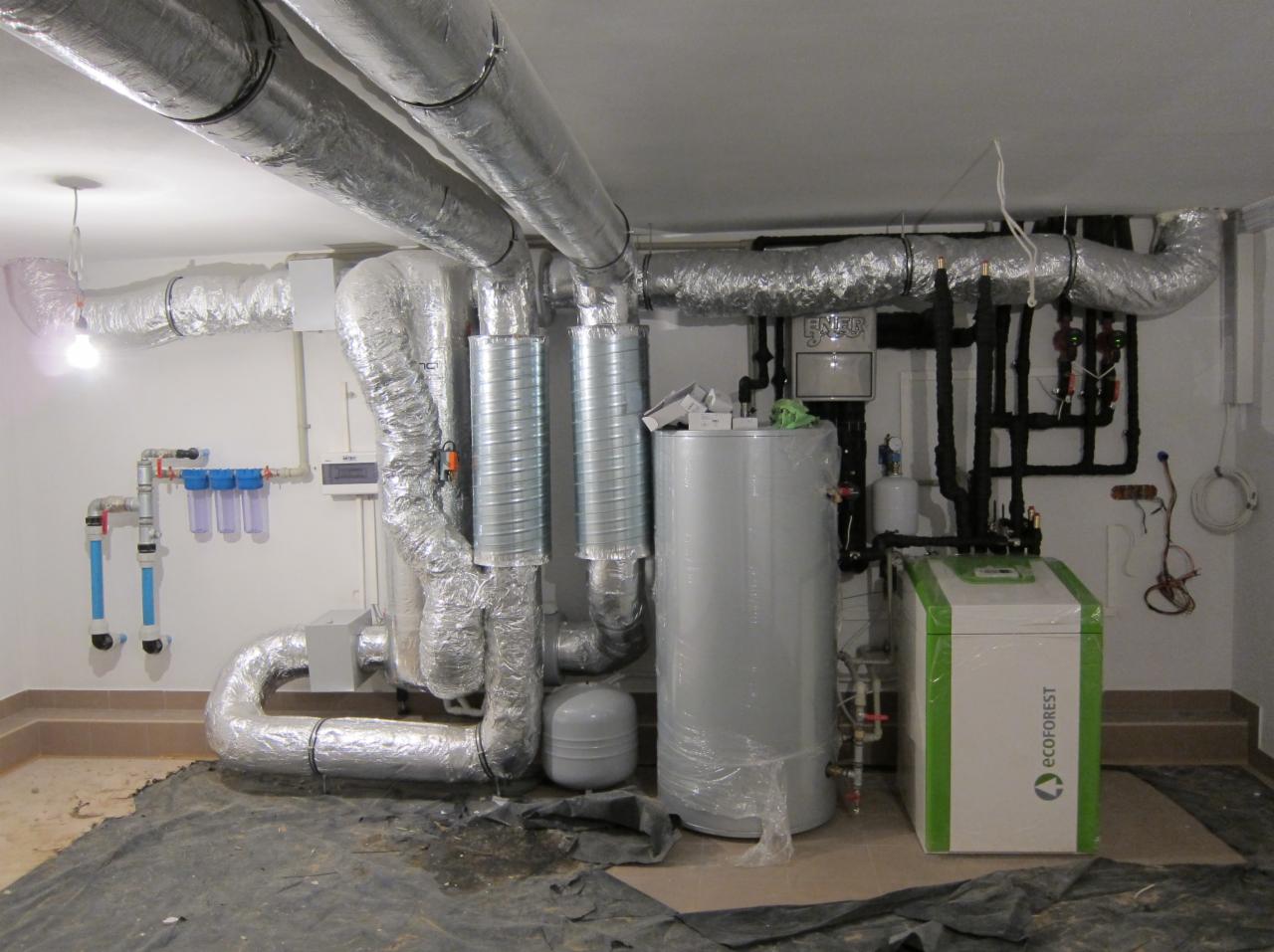 Nowoczesna kotłownia z pompą ciepła Ecoforest, rury w izolacji termicznej, filtry wody i automatyka. Instalacja w piwnicy, widok z przodu.