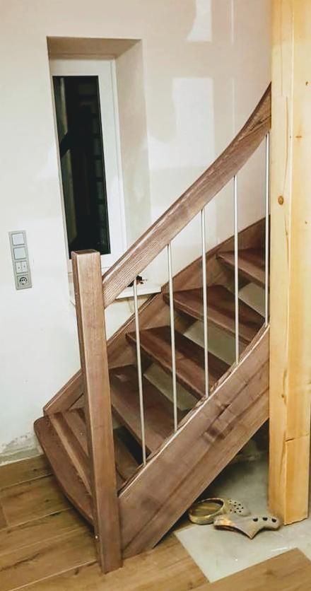 Klatka schodowa z drewna w trakcie montażu, widoczne niedoskonałości wykończenia ścian, drewniane stopnie z metalowymi barierkami, na podłodze robocze obuwie.