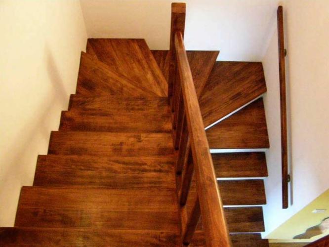 Widok z góry na ciemne, lakierowane stopnie z drewna egzotycznego, z prostą, drewnianą balustradą po prawej stronie, przy białej ścianie.