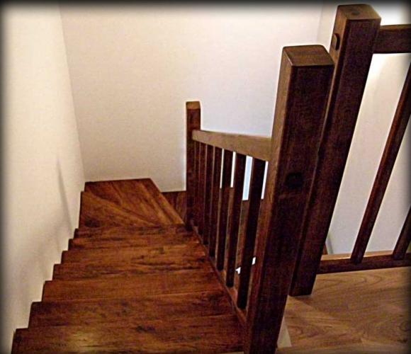 Kątowy widok z góry na ciemne schody z drewna egzotycznego, z masywną balustradą. Widoczne detale połączeń elementów balustrady i unikalny rysunek słojów drewna.