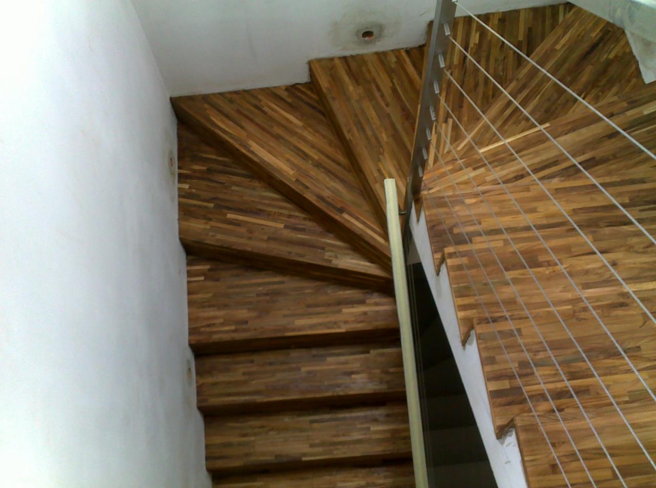 Spiralne schody z drewna egzotycznego, zabezpieczone metalową balustradą z linkami, widok z góry, akcent na naturalne usłojenie drewna.