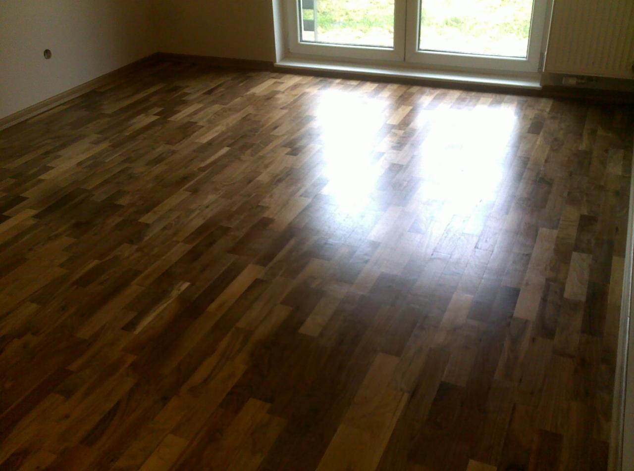 Parkiet ułożony w jodełkę w jasnym pokoju z oknem. Widoczne naturalne usłojenie drewna i refleksy światła, podkreślające gładką powierzchnię podłogi.