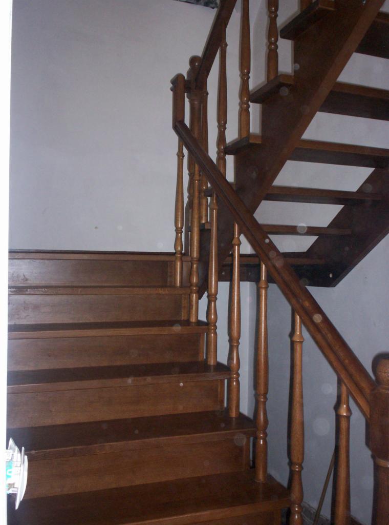 Drewniane schody z balustradą w kolorze brązu, widoczne od dołu, z detalami toczonych słupków i prostych stopni. Naturalne drewno, klasyczny styl.