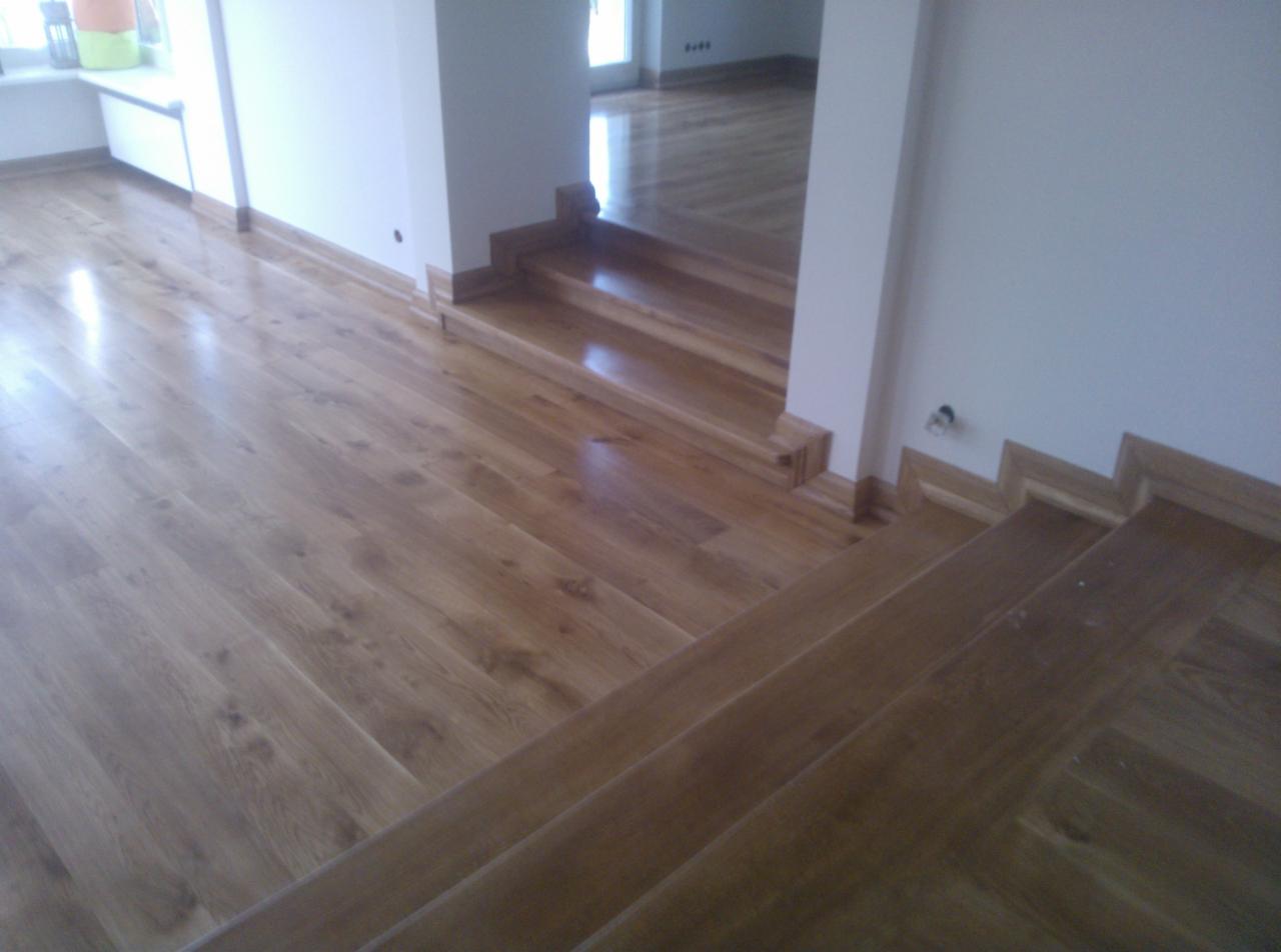 Drewniane schody i podłoga po cyklinowaniu, widoczne detale wykończenia przy ścianach i stopnicach, jasne drewno, wnętrze domu.