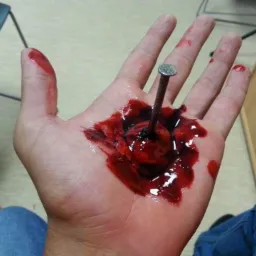 Realistyczna rana dłoni z wbitym gwoździem, używana podczas symulacji urazów na kursie pierwszej pomocy. Krew i sztuczne uszkodzenia skóry.