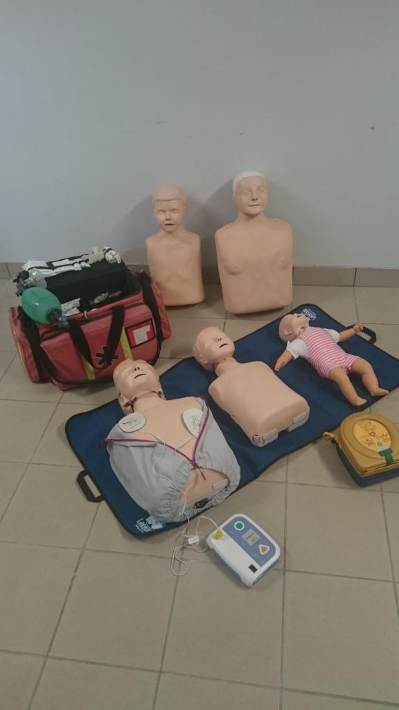 Manekiny szkoleniowe, torba ratownicza i defibrylator na podłodze z płytek. Sprzęt do nauki udzielania pierwszej pomocy, w tym manekin niemowlęcia.