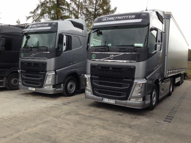 Flota transportowa z Wieliczki: Dwa szare ciągniki siodłowe Volvo Globetrotter, jeden z naczepą, stoją na placu. Widoczne tablice rejestracyjne.