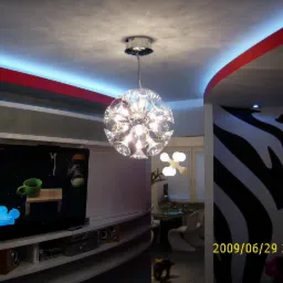 Nowoczesny salon z dekoracyjnym oświetleniem sufitowym i ścianą w zebrę. Widoczny telewizor, meble w zabudowie i designerska lampa wisząca.