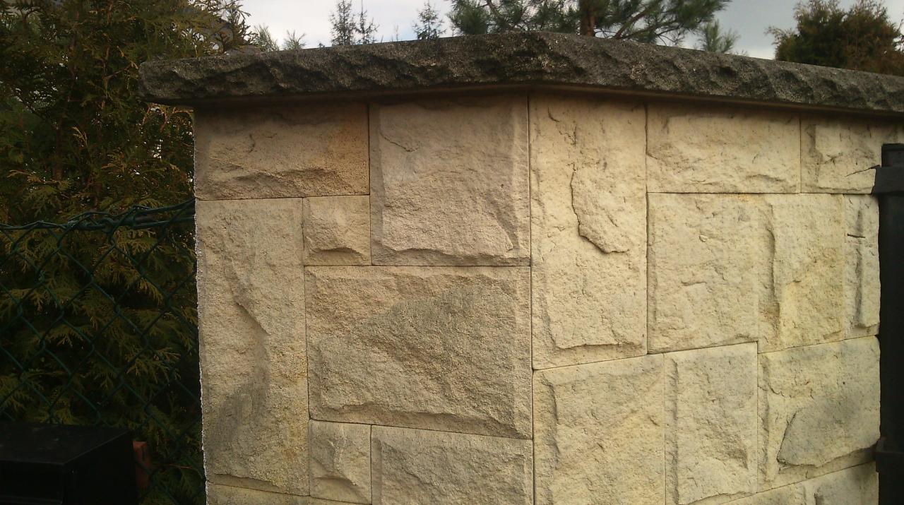 Fragment ogrodzenia z piaskowca w Jasienicy, z widoczną fakturą kamienia i zielenią w tle.