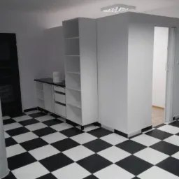 Wnętrze po remoncie z czarno-białą podłogą w szachownicę, białe meble zabudowane pod ścianą, widoczny fragment drzwi przesuwnych do innego pomieszczenia.