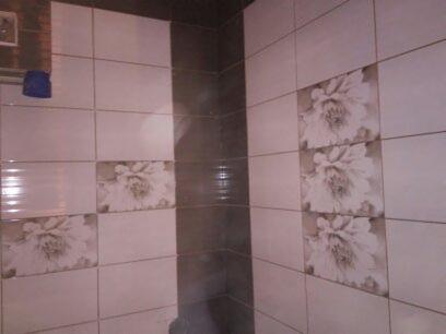 Wykończona łazienka z jasnymi, kwadratowymi płytkami z motywem kwiatowym, uzupełniona pionowym pasem ciemniejszych płytek w rogu.