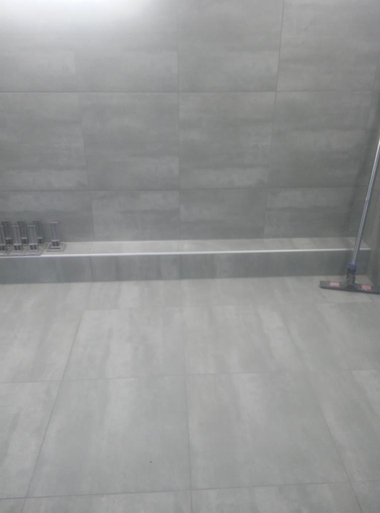 Świeżo położone szare płytki podłogowe i ścienne, widoczne narzędzia glazurnicze i mop do czyszczenia fug.