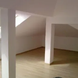 Poddasze po remoncie z jasnymi panelami podłogowymi, pomalowane na biało, z widocznymi skosami i oknem dachowym.