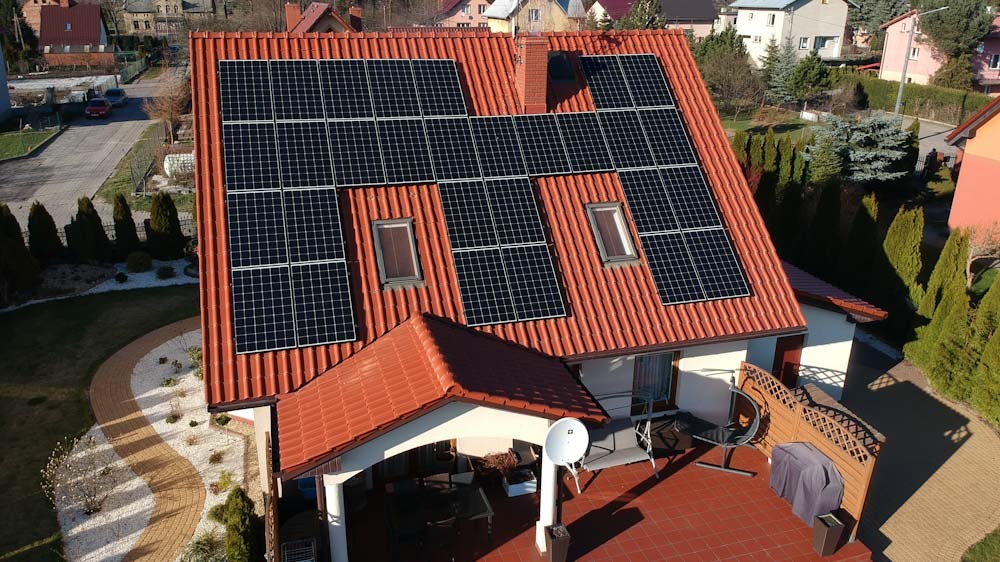 Czerwony dach z panelami słonecznymi, widoczne okna dachowe i antena satelitarna, ujęcie z góry.