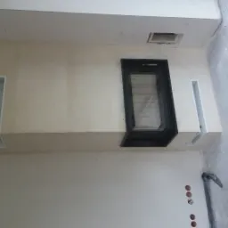 Fragment ściany z wnęką na wkład kominkowy z czarną obudową, widoczne otwory wentylacyjne i instalacja elektryczna, stan surowy przed wykończeniem.