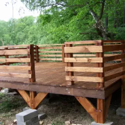 Drewniany taras z balustradą, świeżo zaimpregnowany, na betonowych podstawach, z widokiem na zielony las.