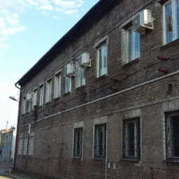 Zewnętrzne jednostki klimatyzacji zamontowane na starej, ceglanej elewacji budynku biurowego z kratami w oknach.