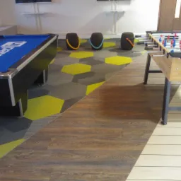 Nowoczesna podłoga: wykładzina dywanowa w heksagony (szary, żółty) łączy się z panelami drewnopodobnymi w pokoju rekreacyjnym z bilardem i piłkarzykami.