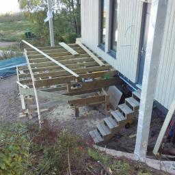 Zygmunt Zumowicz - Konstrukcja drewniana pod przyszły taras przy budynku z drewnianą elewacją, widoczne schody wejściowe, teren wokół w trakcie prac ziemnych.