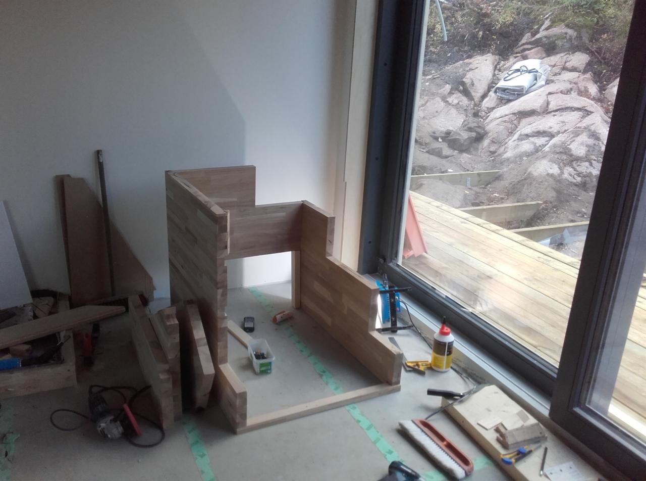 Montaż drewnianej zabudowy okiennej z widokiem na taras w trakcie budowy, narzędzia i materiały rozłożone na podłodze.