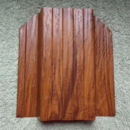 Próbka panela elewacyjnego z tworzywa sztucznego imitującego drewno, widoczne pionowe żłobienia i struktura drewna, ułożona na teksturowanym tle.