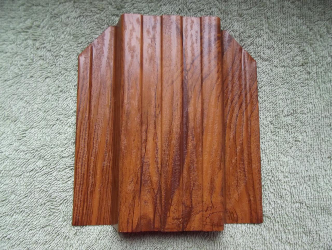 Próbka panela elewacyjnego z tworzywa sztucznego imitującego drewno, widoczne pionowe żłobienia i struktura drewna, ułożona na teksturowanym tle.