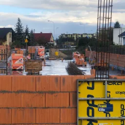 Wznoszenie ścian z cegły ceramicznej na mokrym fundamencie, widoczne szalunki Doka Frami Xlife i zbrojenie pionowe, teren budowy z materiałami CERPOL