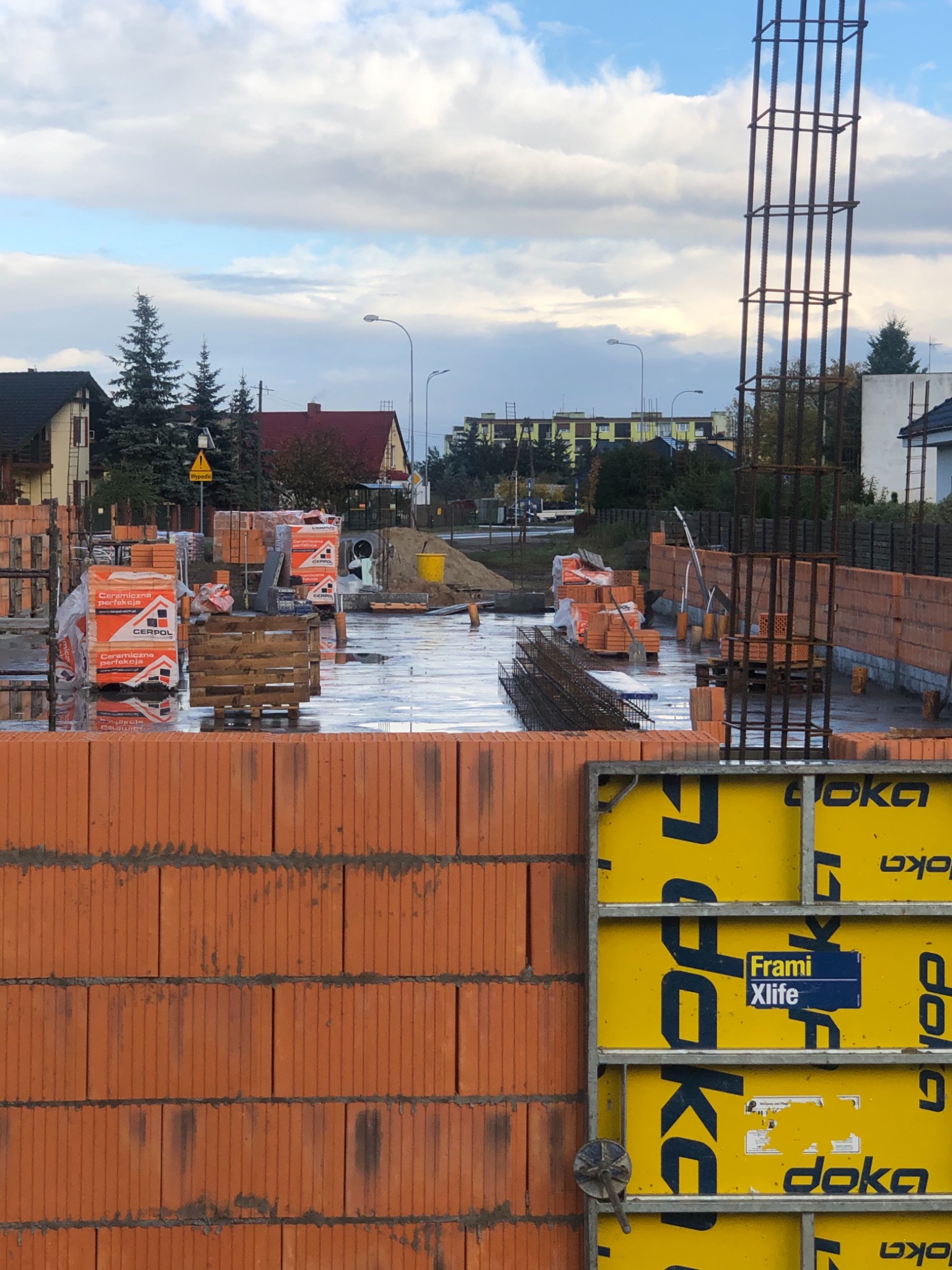 Wznoszenie ścian z cegły ceramicznej na mokrym fundamencie, widoczne szalunki Doka Frami Xlife i zbrojenie pionowe, teren budowy z materiałami CERPOL