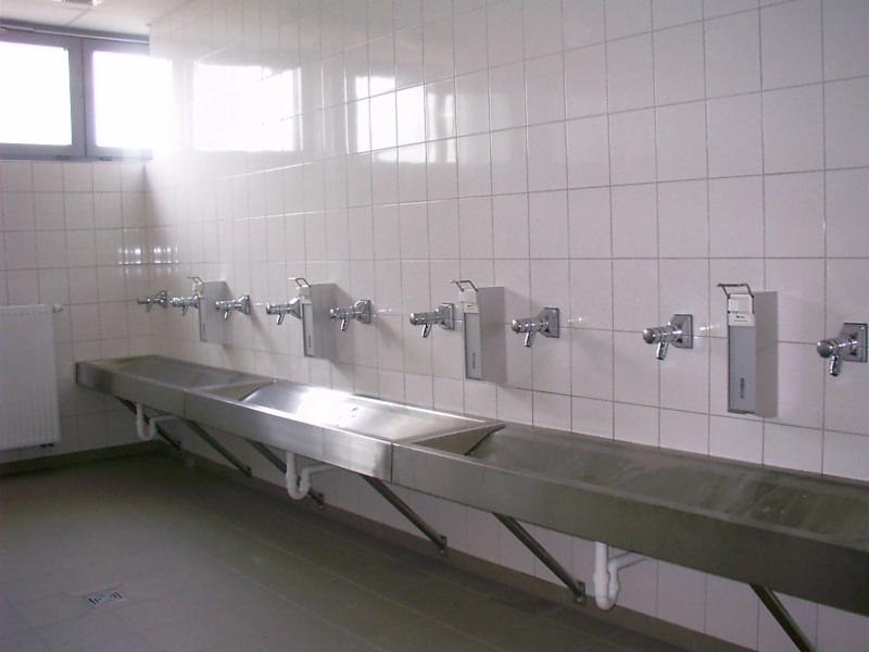 Rząd umywalek ze stali nierdzewnej z dozownikami mydła zamontowanymi na kafelkowanej ścianie w publicznej toalecie.