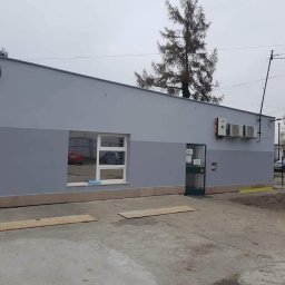 BOA Rafał Duś - Dwukolorowa szara elewacja budynku z zamontowanymi klimatyzatorami, widoczna z poziomu betonowego placu z drewnianymi deskami zabezpieczającymi podłoże.