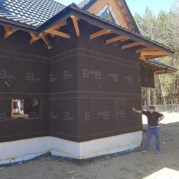 BOA Rafał Duś - Dom w trakcie ocieplania: widoczna warstwa izolacyjna z czarną membraną Aqua Control XXL, styropian przy gruncie, drewniana konstrukcja dachu i mężczyzna wskazujący na ścianę.