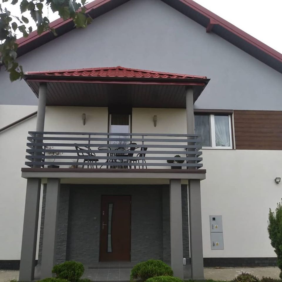 Dom z balkonem po remoncie elewacji: szara góra, kremowa ściana z brązowymi akcentami, ciemnoszara balustrada balkonu i kolumny.