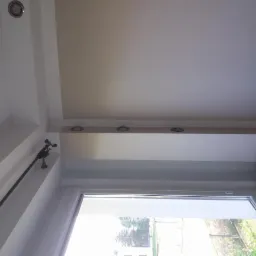 Widok sufitu z oświetleniem punktowym LED, karniszem i oknem z widokiem na zieleń.