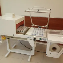 Automatyczna maszyna do pakowania w folię termokurczliwą, z widocznymi zapakowanymi produktami na taśmie transportowej, marki Turpak i Tech-Pack.