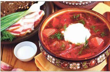 Apetyczny, gorący barszcz ukraiński w ozdobnej misce, z kleksem śmietany i koperkiem, obok pieczywo, boczek i zielony szczypior. Idealne danie na catering.