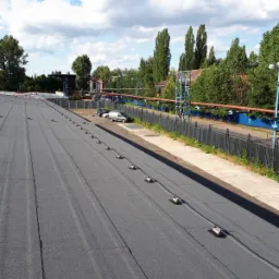 Płaski dach pokryty papą z zamontowanymi uchwytami odgromowymi, widok z góry w słoneczny dzień.