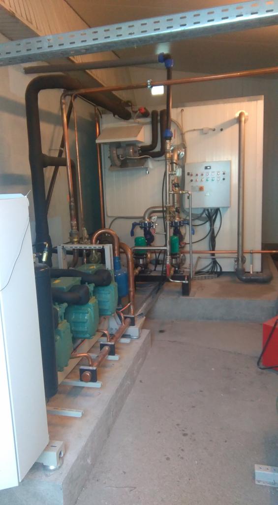 Instalacja chłodnicza z rurami miedzianymi, zielonymi sprężarkami i panelem sterowania w pomieszczeniu technicznym w Strzegowie.