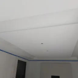 Biały sufit podwieszany z płyty karton gips, widok z dołu, niebieska taśma malarska wzdłuż krawędzi ścian, przygotowanie do malowania.