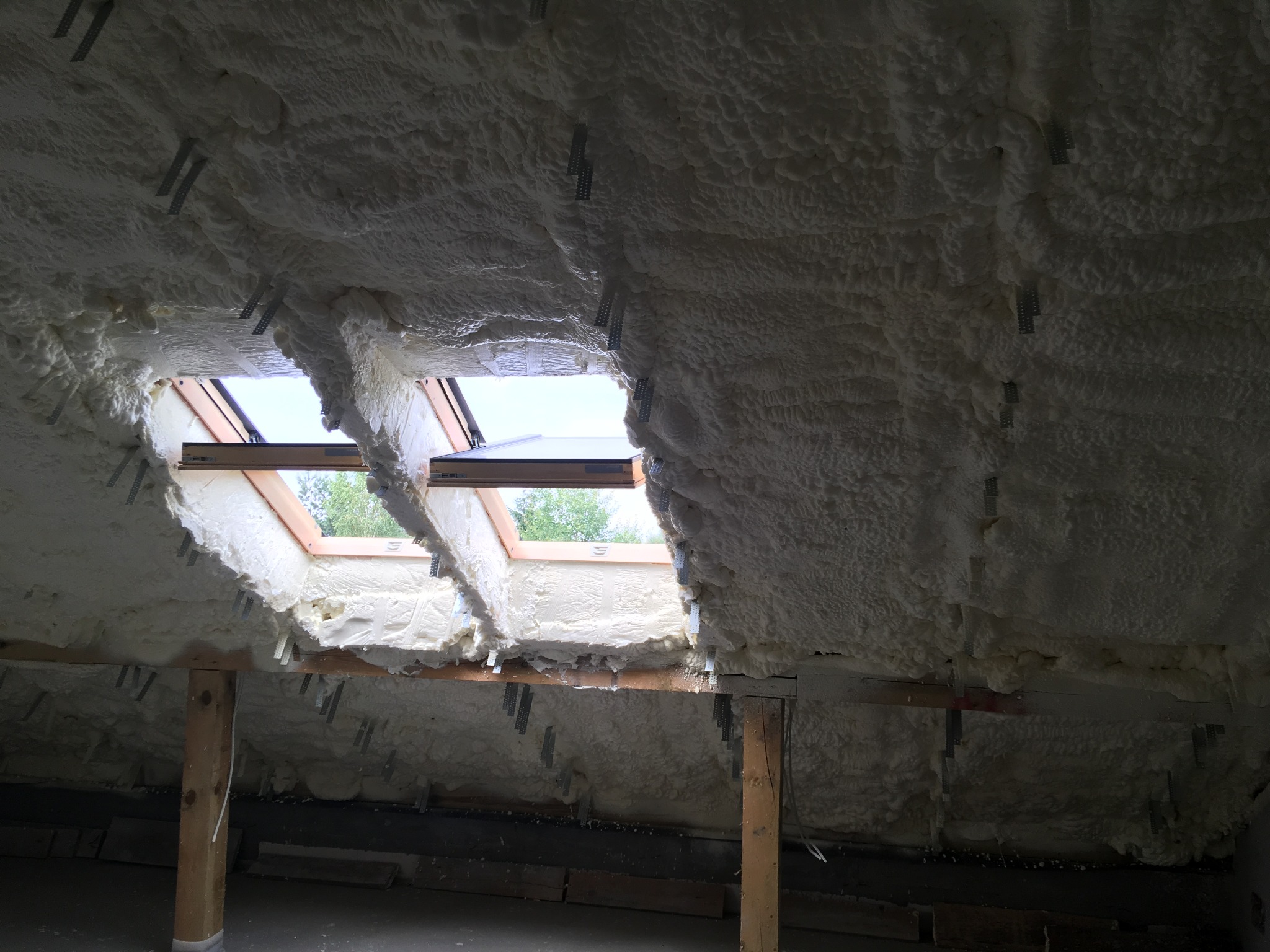 Poddasze z oknami dachowymi po ociepleniu pianą poliuretanową, widoczne metalowe łączniki mocujące izolację.