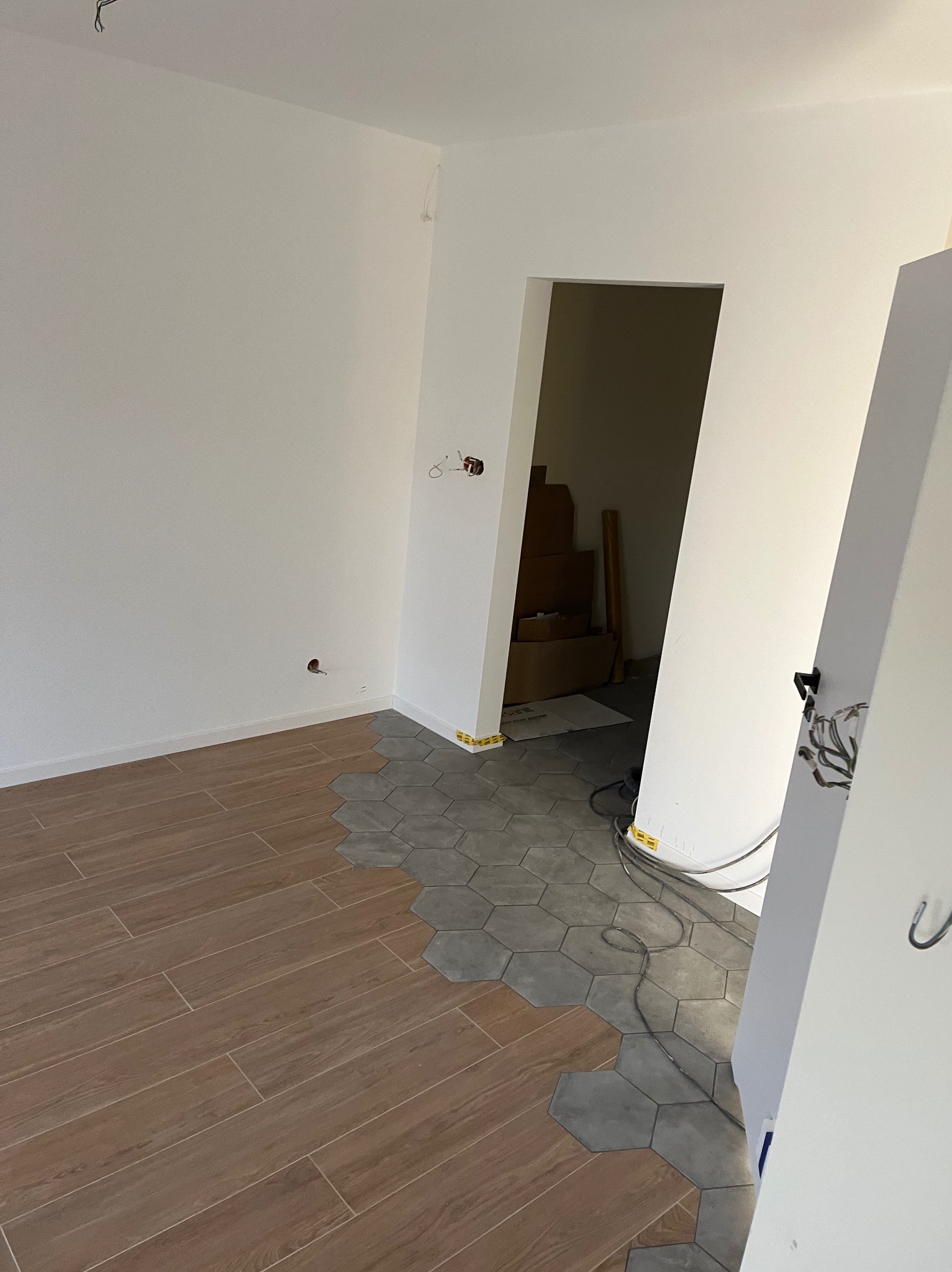 Układanie podłogi w Wieluniu: połączenie drewnopodobnych paneli i szarych heksagonalnych płytek, widoczne kable i przygotowane podłoże w przejściu do innego pomieszczenia.