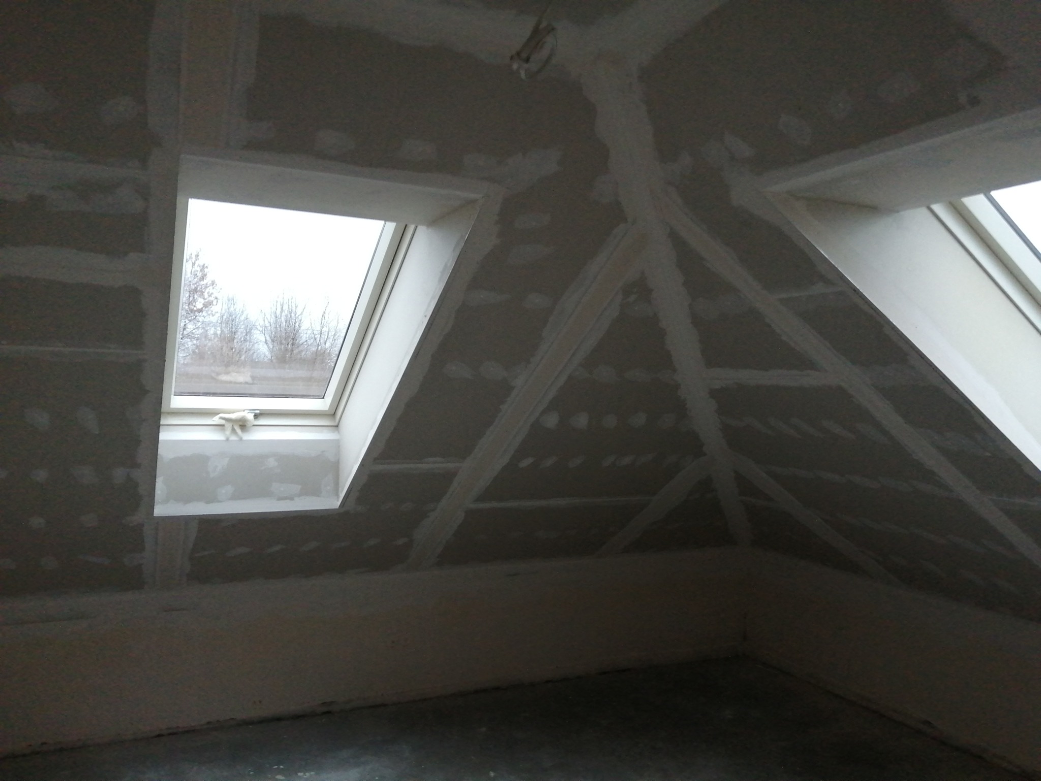 Poddasze z oknami dachowymi, wykończone płytami karton-gips, szpachlowane łączenia. Widoczne elementy konstrukcyjne dachu. Etap prac wykończeniowych.