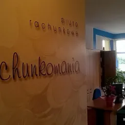 Wnętrze biura rachunkowego 'Rachunkomania' z dekoracyjną ścianą, widoczne stanowiska pracy i okna. Jasne, przestronne pomieszczenie z elementami niebieskiego koloru.